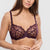 A woman modeling a matching lingerie set in deep plum purple, featuring sheer polka-dot cups on the bra and floral lace detailing on the panties, against a light gray studio background.