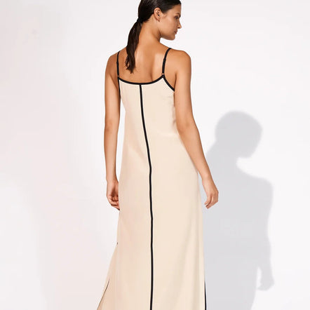 A woman modeling a long cream maxi slip dress with black trim, shown from the back against a white studio background.