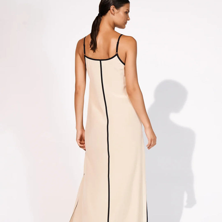 A woman modeling a long cream maxi slip dress with black trim, shown from the back against a white studio background.