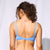 A woman shown from the back wearing a light blue textured bikini set against a white studio backdrop.