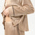 A close-up of a person wearing a beige satin pajama set with black piping trim, including a long-sleeve button-front top and matching pants.