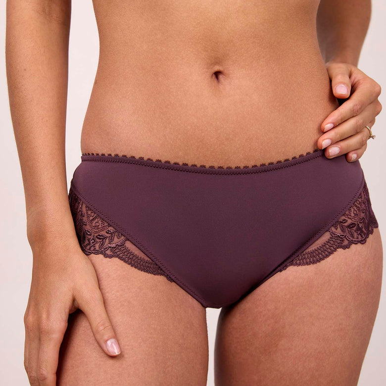Person wearing a pair of dark purple lace underwear on a plain background