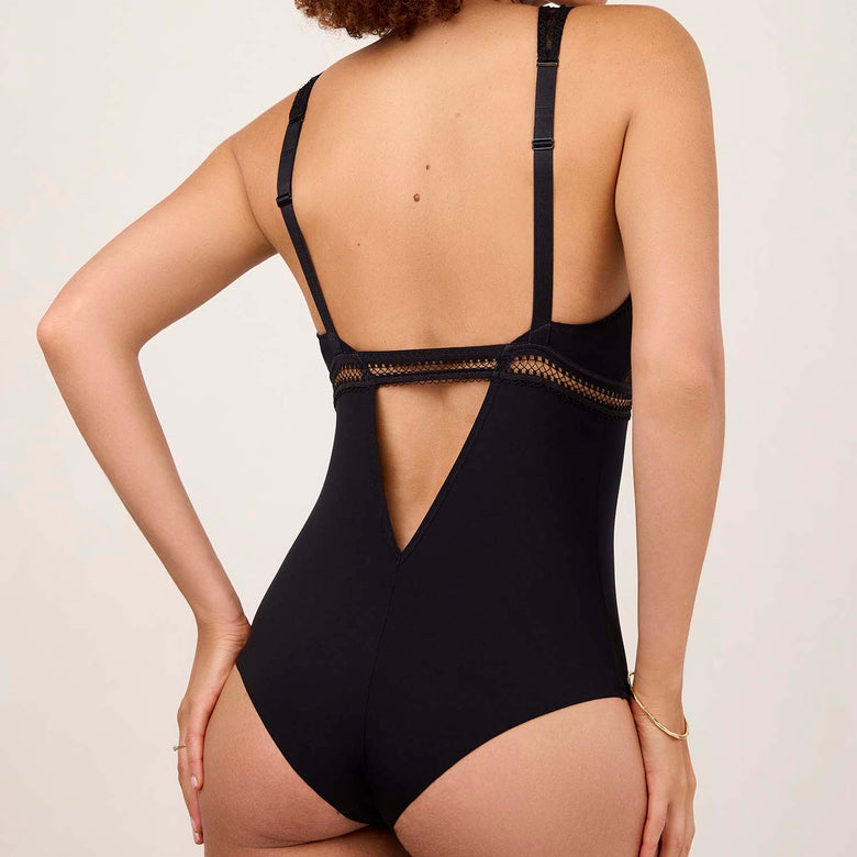 Woman wearing a black lace bodysuit against a plain background