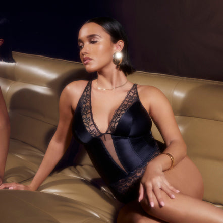 Woman in a black lace bodysuit sitting on a beige couch.
