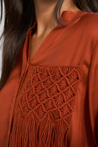 Close-up of a rust-colored blouse with intricate lace detailing on a plain background