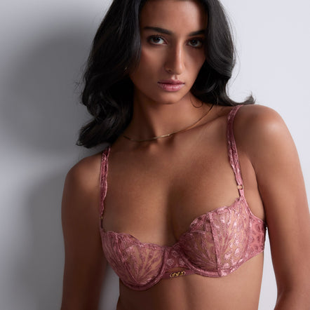 Woman wearing a pink lace bra against a plain background