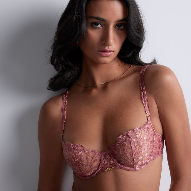 Woman wearing a pink lace bra against a plain background