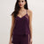 A woman modeling a matching two-piece loungewear set in deep plum purple, featuring a camisole top with lace side panels and coordinating shorts with lace side panels, against a plain light background.