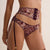 A close-up of a model wearing a sheer floral lace lingerie set with a garter belt and attached garter straps with gold-tone hardware, against a solid light beige background.