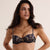 A woman modeling a two-piece lingerie set featuring a dark navy blue base with an intricate paisley pattern in gold, beige, and brown, set against a solid light beige background.