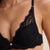 Close-up of a model wearing a black lace bra with gold-tone hardware and a small decorative charm at the center front.