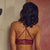 A woman stands with her back to the camera wearing a burgundy lace lingerie set in a room with a fireplace and a large red artwork on the wall.