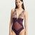 A model wearing a deep purple lace and sheer mesh one-piece bodysuit against a plain light gray studio background.