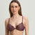 A woman modeling a matching lace lingerie set in a deep plum purple color, featuring a sheer underwire bra and high-waisted briefs, against a plain light gray studio background.