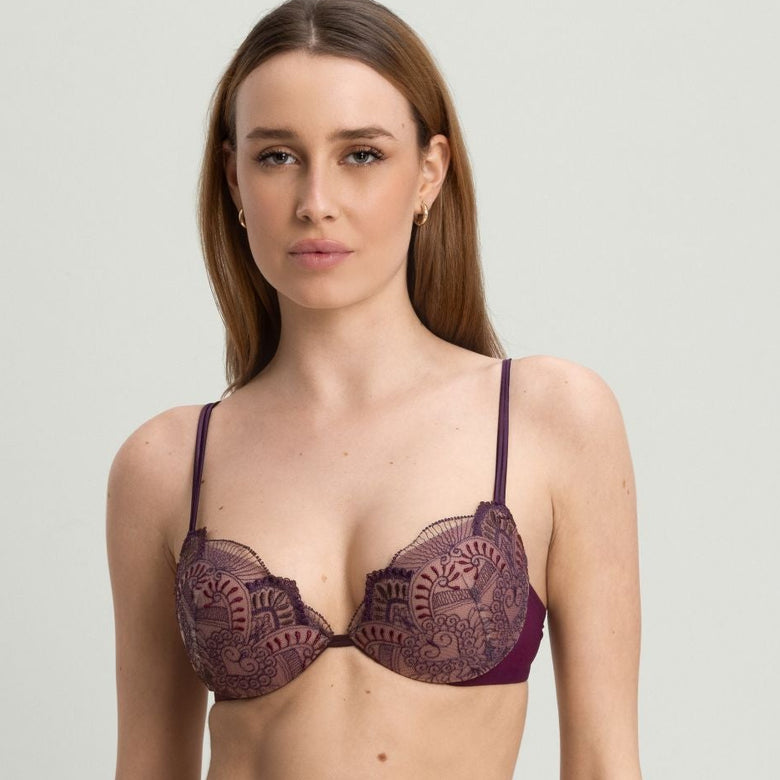 A woman modeling a matching lace lingerie set in a deep plum purple color, featuring a sheer underwire bra and high-waisted briefs, against a plain light gray studio background.