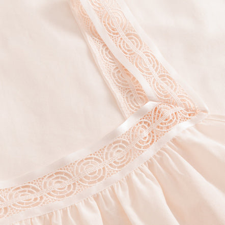 Close-up of a light pink dress with lace detailing on a soft beige background