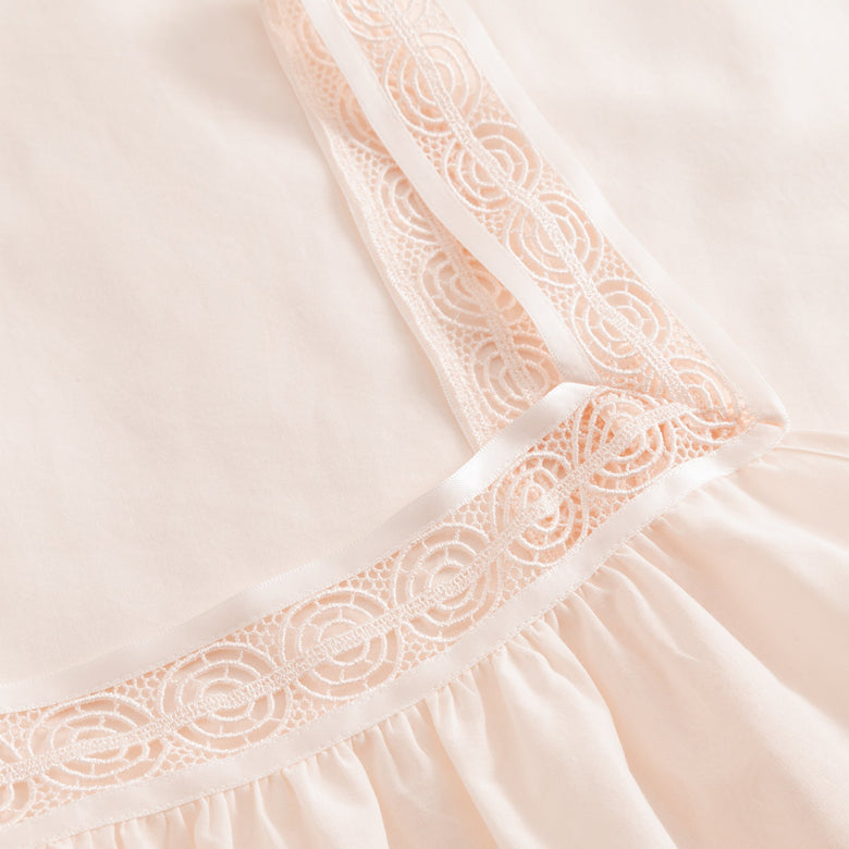 Close-up of a light pink dress with lace detailing on a soft beige background