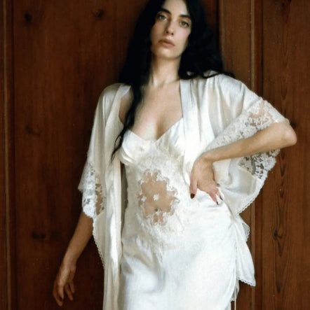 Woman wearing a white lace nightgown and robe against a wooden background