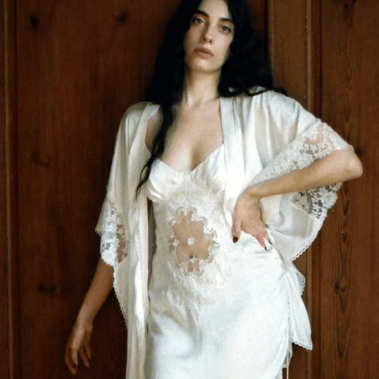 Woman wearing a white lace nightgown and robe against a wooden background