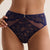 A close-up of a model wearing navy blue lace high-waisted briefs with sheer mesh side panels and a small gold clasp at the center front, against a plain light beige background.
