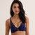 A woman modeling a navy blue lace lingerie set consisting of a bralette with a front zipper and matching high-waisted briefs, set against a plain beige studio background.