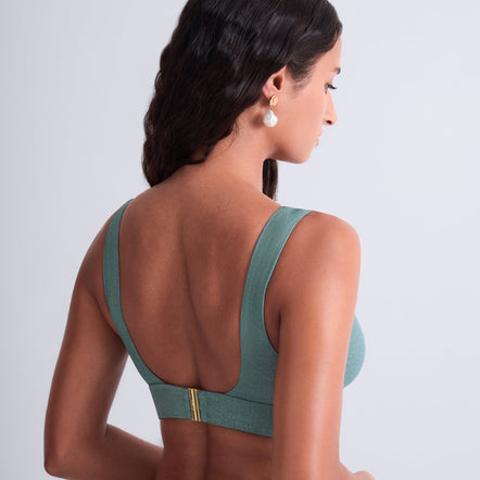 Woman wearing a green sports bra and leggings on a light gray background