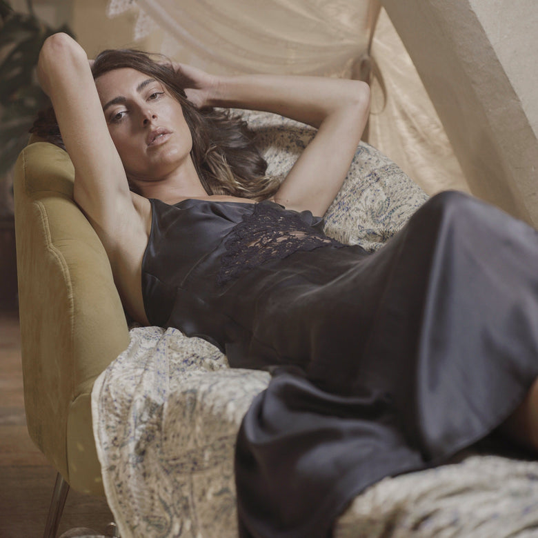 Woman in a black dress lying on a patterned chair with a disco ball in the foreground.