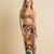 Woman wearing a floral sarong and brown bikini top against a beige background