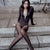 A woman sits on stone steps wearing a dark brown long-sleeve bodysuit with a plunging neckline, sheer black tights, and black pointed shoes.