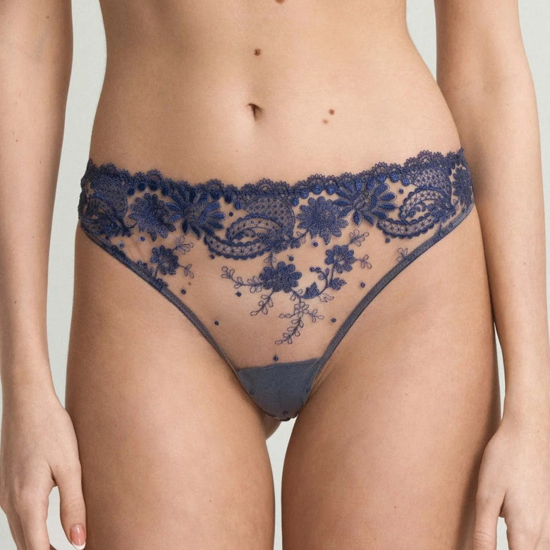 A close-up of a model wearing a navy blue lace lingerie set, featuring a sheer floral lace high-waisted brief and a matching bra top, against a light gray background.