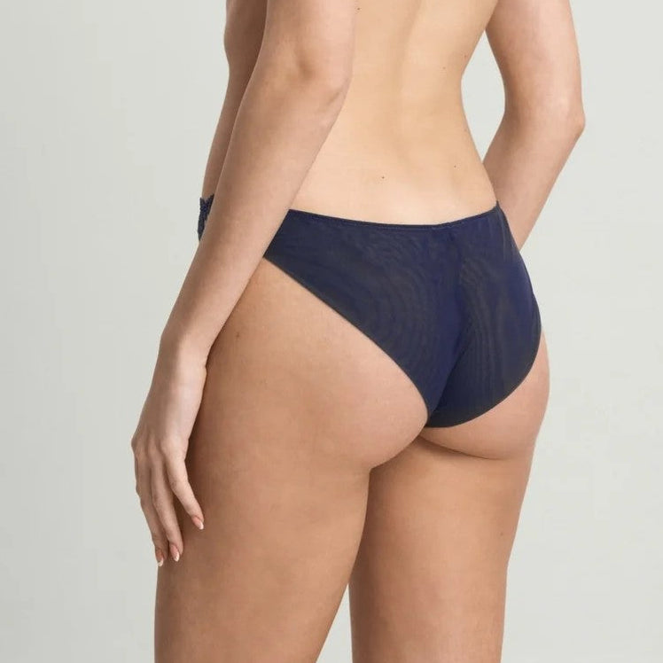 A woman modeling a navy blue lace lingerie set, shown from a side-back angle against a plain light gray studio background.