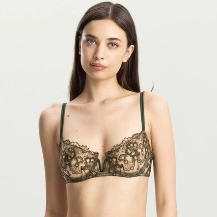 A woman modeling a dark olive green lace lingerie set against a light gray studio background.