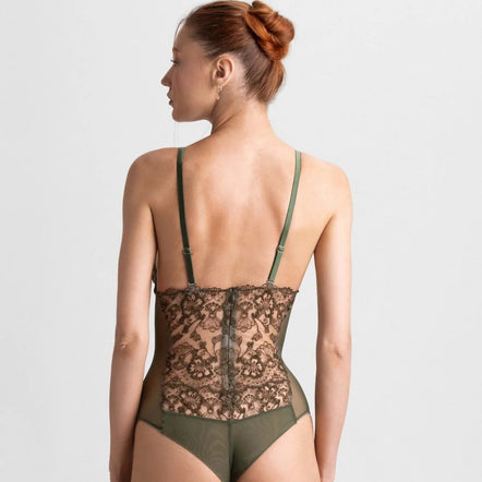 A woman shown from the back wearing a lace and mesh one-piece bodysuit with olive green straps and matching bottoms, photographed against a light gray studio background.