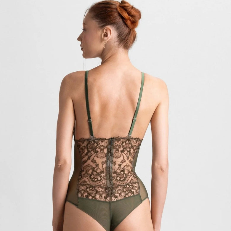 A woman shown from the back wearing a lace and mesh one-piece bodysuit with olive green straps and matching bottoms, photographed against a light gray studio background.
