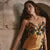 A woman wearing a satin slip dress with dark blue floral lace trim, leaning against a stone wall in a rustic setting.