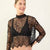A woman modeling a sheer black floral lace mock-neck long-sleeve top over a black bralette, paired with black underwear, against a plain off-white studio background.