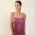 A woman modeling a short satin slip dress in a dusty mauve-purple color, standing against a plain off-white background.