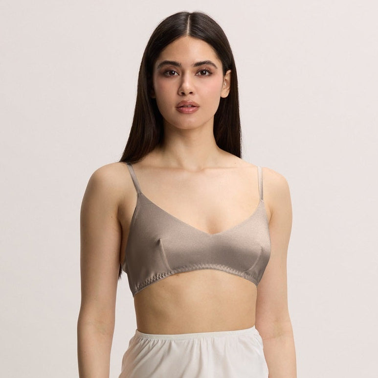 Woman wearing a beige bralette and white lace-trimmed skirt on a plain background