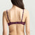 A woman shown from the back wearing a sheer burgundy lace lingerie set with matching thigh-high stockings against a light gray studio background.