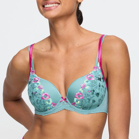 Woman wearing a teal bra with floral embroidery and pink straps on a plain background
