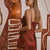 A woman wearing a short burgundy satin slip dress with lace trim, standing in front of a stylized brown and white wall mural.