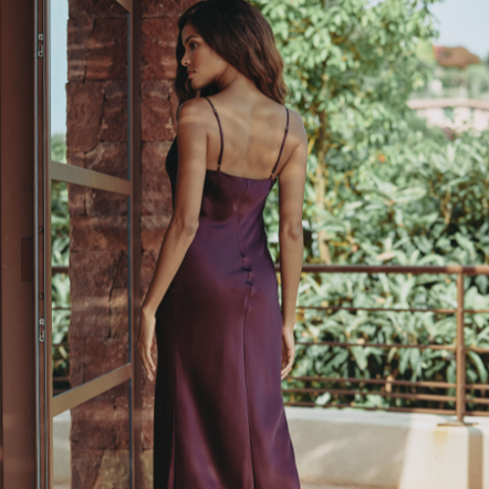 Woman in a purple dress standing on a wooden deck with greenery in the background