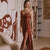 A woman models a long, red lace slip dress with a thigh-high slit in a modern, stylishly decorated room with a beige sofa and wooden table.