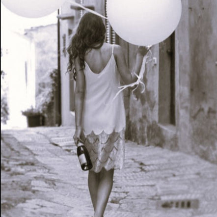 Woman holding white balloons walking down a street