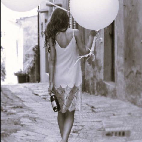 Woman holding white balloons walking down a street